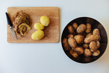 Potato knife and peeling on a wooden plank on a white kitchen table