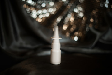 little white plastic bottle nasal spray for nozzles and illness with copy space, place for text, company name on satin dark gray background with bokeh