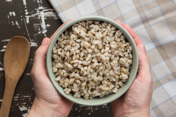 Top view of woman hands holding bowl with pearl barley porridge on the wooden surface