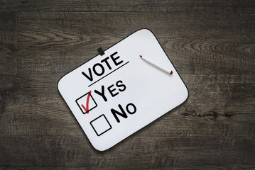 White board with the word Vote,Yes  and No Check boxes ,on a dark wooden background