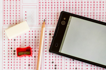 Smart phone with blank screen,wooden pencil,eraser and sharpener on exam sheet,education concept.