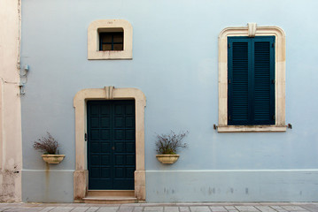 Fototapeta na wymiar The fachade of a blue old Italian house with green door and windows, Castro, Puglia