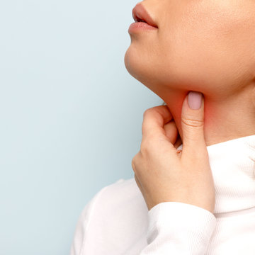 Close up of woman touches fingers of sore throat, isolated on grey background. Thyroid gland, painful swallowing, tonsillitis, laryngeal swelling concept. Inflammation of the upper respiratory tract