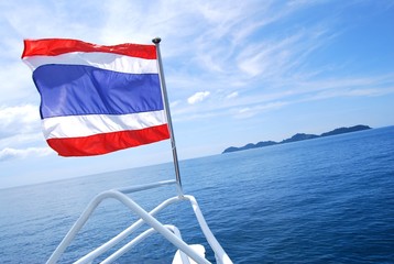 The flag of Thailand is in front of the ship. Have a beautiful island and sea background.