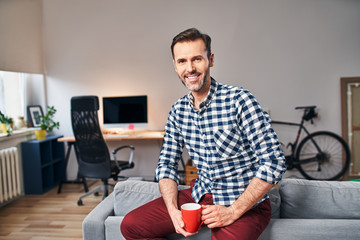 Portrait of adult man sitting on sofa with cup of coffee in his home office