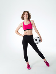 Full length, young athletic woman with a soccer ball in her hands, standing against a gray background and looking at the camera.