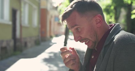 Portrait of man sneezing strongly and spraying nose with nasal spray on street