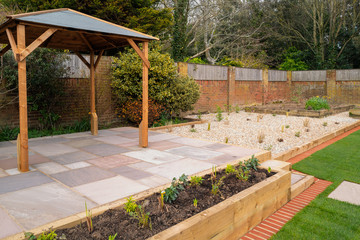 A new raised patio with a wooden gazebo in front of a raised flowerbed and a gravel garden area. - obrazy, fototapety, plakaty
