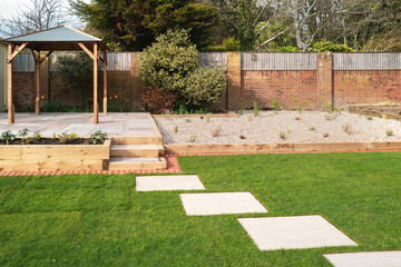 New stepping stones leading to steps and a raised patio with a wooden gazebo, next to a gravel...