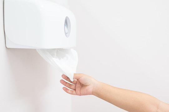 Close Up Woman Hand Picking White Toilet Tissue Paper For Cleaning Hand On White Wall Background.Right Hand Pull Tissue From White Plastic Box After Hand Wash In Bathroom.