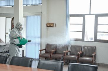 Disinfecting of office to prevent COVID-19, person in white hazmat suit with disinfect in office, coronavirus concept