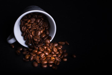  Brown coffee beans coming out of a white cup on a black background. Horizontal format.