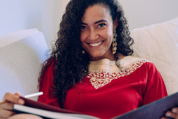 Obraz premium Beautiful ethnic woman writing on a notebook at home. Moroccan female with traditional clothes with copyspace. African culture indoors at the house. Portrait of young female with muslim lifestyle.