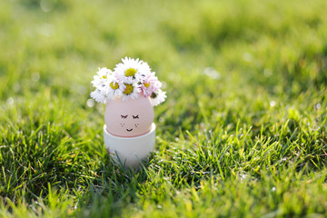 Cute egg with face and flowers wreath. Easter still life. Easter egg concept. Spring is coming. Minimal holiday concept. Cute creative photo. 