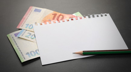 Blank note paper, euro banknotes and pencil on blackboard, chalkboard black