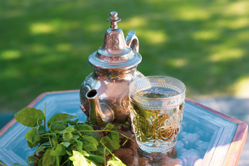 Detail of moroccan cold green herbal tea on a traditional tray. Healthy detox clear beverage. Arabian culture and traditions. Muslim lifestyle at home. Organic fresh moroccan hot infusion on a glass..