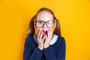 Shocked school girl in glasses looking at camera on yellow background © Elena Kratovich
