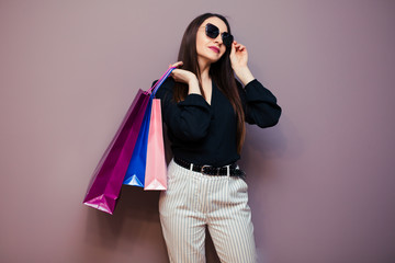 Portrait of excited pretty girl in blouse and sunglasses holding shopping bags isolated on purple background