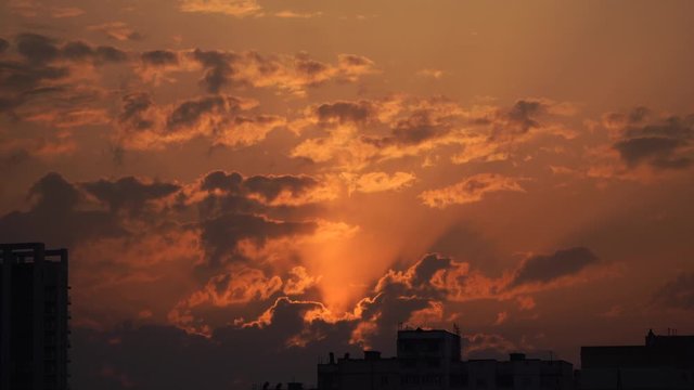 Urban silhouette with a dramatic sunset orange clouds and sun disk 