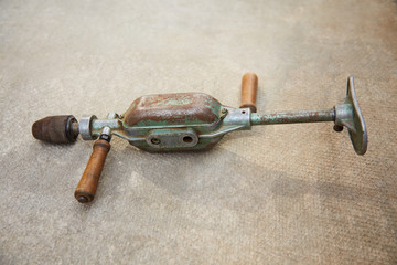 Old mechanical rusty drill General plan. It lies on a gray concrete surface. Side view