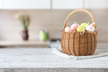 Wicker basket with easter colorful eggs on kitchen wooden table. Spring easter composition. Space for text.