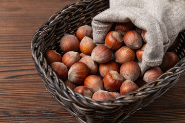 Lots of hazelnuts in shells in a wooden basket, close up. Old brown wooden table