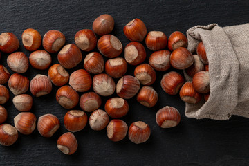 Hazelnuts in shells fall out of a linen bag on a black background with texture.