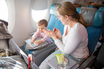 a little cute toddler girl sitting in an airplane in a chair by the porthole herself wipes a...