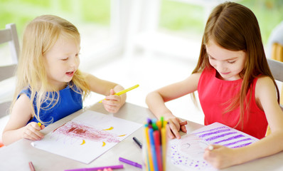 Two sisters drawing with colorful pencils at home. Creative kids doing crafts together. Education and distance learning for kids. Homeschooling during quarantine. Stay at home entertainment.