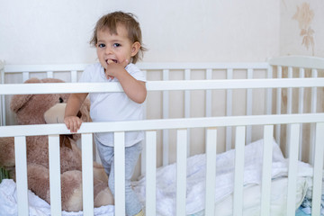 coronavirus covid-19  quarantine concept. take time with your family. little cute toddler is standing in the crib and looking at the camera smiling cheerfully