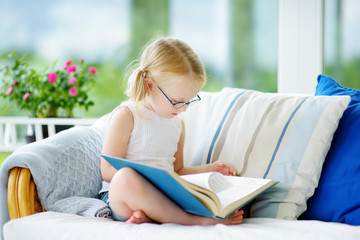 A girl reading a book in living room. Smart schoolgirl doing her homework after school. Education...