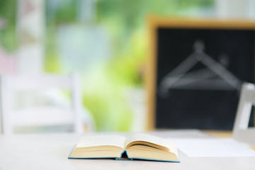 Open book laying on white desk in a classroom. Open textbook in front of a blackboard. Education and distance learning for kids. Homeschooling during quarantine.