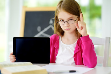 Smart schoolgirl doing her homework with digital tablet at home. Child using gadgets to study. Education and distance learning for kids. Homeschooling during quarantine.