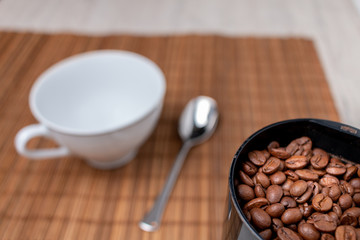 Coffee beans in a electric coffee grinder on a table with a coffee mug. 