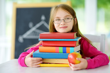 Smart schoolgirl studying with a pile of books on her desk. Young girl doing her homework. Education and distance learning for kids. Homeschooling during quarantine.