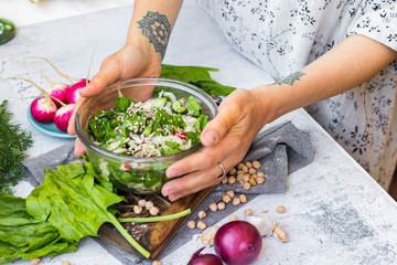 Detox vitamin green fresh salad in bowl. Mix of vegetables, sesame seeds and herbs, spinach in young woman's hands.