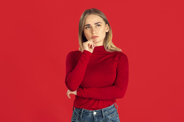 Thinking. Monochrome portrait of young caucasian blonde woman isolated on red studio background. Beautiful female model in shirt. Human emotions, facial expression, sales, ad concept. Youth culture.