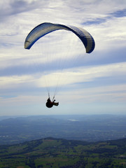 &Eacute;pine mountain, France - August 5th 2008 : Focus on a blue and white paraglider in mid flight. We can see the green countryside of the French Alps in the background.