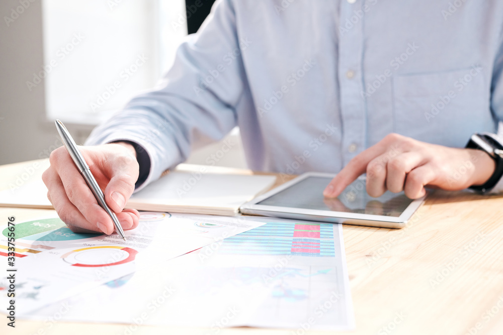 Aufkleber Close-up of unrecognizable financier sitting at desk and using tablet while analyzing graphs in office