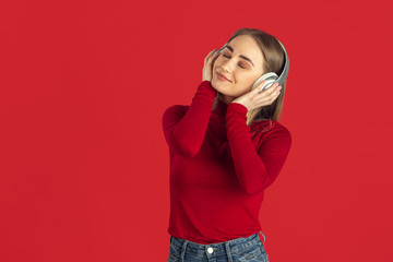 Listen to music. Monochrome portrait of young caucasian blonde woman isolated on red studio background. Beautiful model in shirt. Human emotions, facial expression, sales, ad concept. Youth culture.