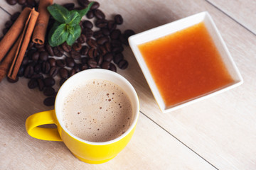 Close-up natural aromatic coffee beans and cup of coffee. Cinnamon sticks, jam, and mint branch. Food texture. Empty space for text.