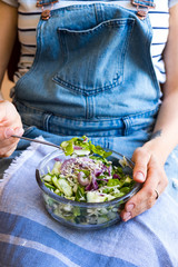 Detox vitamin green fresh salad in bowl. Mix of vegetables and herbs. Cucumbers, red onion, salad leaves. Woman holds in hands on legs bowl of vegan salad. Healthy food.