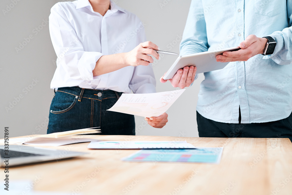 Poster close-up of unrecognizable man holding tablet while discussing marketing plan with colleague in offi