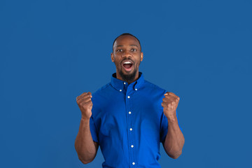 Celebrating win. Monochrome portrait of young african-american man isolated on blue studio...