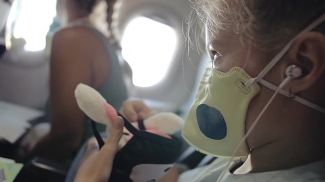 Little girl caucasian at plane with wearing protective medical mask. Child baby tourist at aircraft with respirator play and paint. Coronavirus epidemic sars-cov-2 covid-19 2019-ncov.