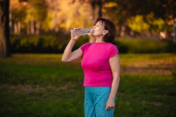 Elderly woman Drinking water from a bottle at sunset