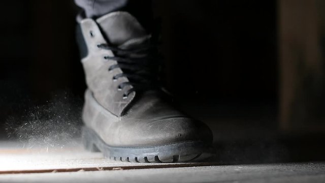 a man walks past the camera, raising dust in the attic into the air. Boot closeup, slow motion