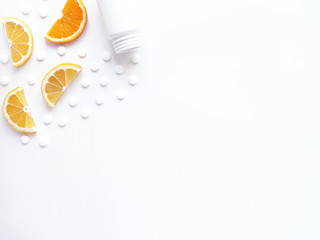 scattered vitamin pills and bottle with lemon orange on white background. Copyspace, flat lay. Concept boost immune system, medicine and tablets.