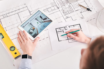 Above view of architect using digital tablet and blueprints while working on floor plan of flat