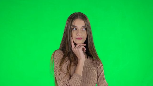 Portrait of slender girl with long hair is daydreaming and smiling looking up on a green screen